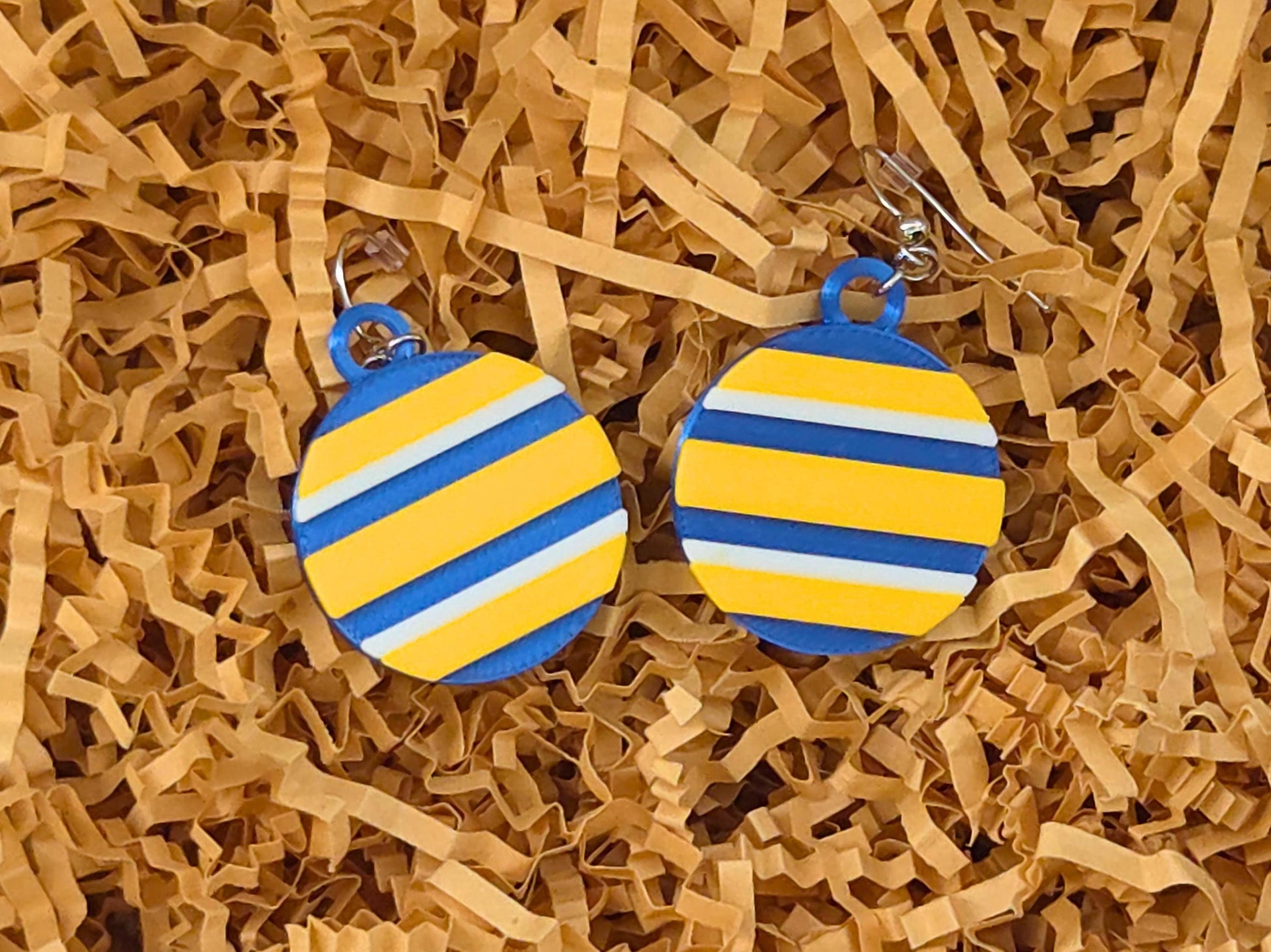 Handmade Buffalo hockey team color earrings resting on tan crinkle paper, perfect for game day gift packaging.