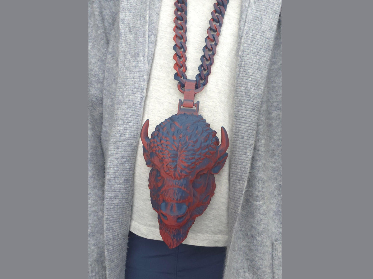 A person wearing a large red and blue buffalo head necklace over a white t-shirt and grey cardigan.